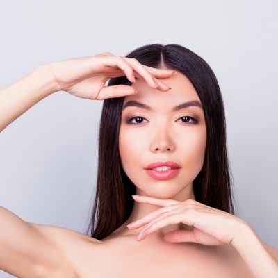 Beauty, health woman  concept. Young pretty chinese lady is touching gently her attractive healthy skin of the face with fingers