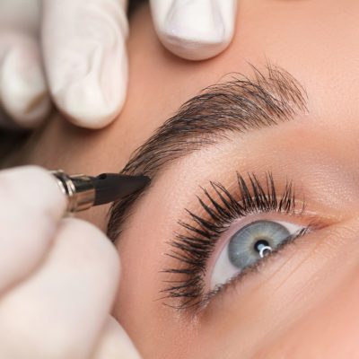 Permanent eyebrow makeup. Cosmetologist applying tattooing of eyebrows. Close up shoot.